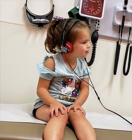 Young girl sitting in exam room with headphones on Aural Habilitation